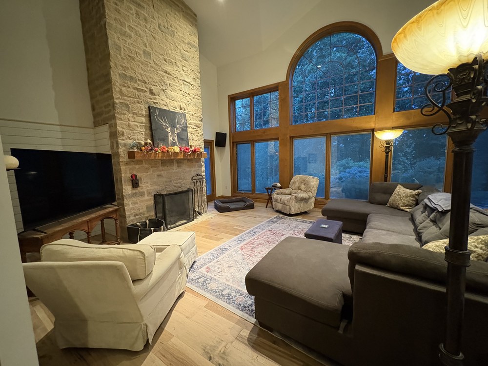 Before: vaulted great room with a dark sectional, patterned recliner, and mismatched decor in front of the stone fireplace